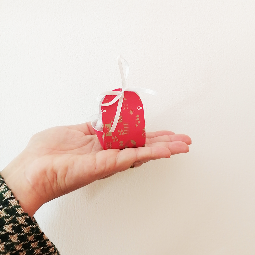 Pequena caixa vermelha decorada com fita branca em mão feminina