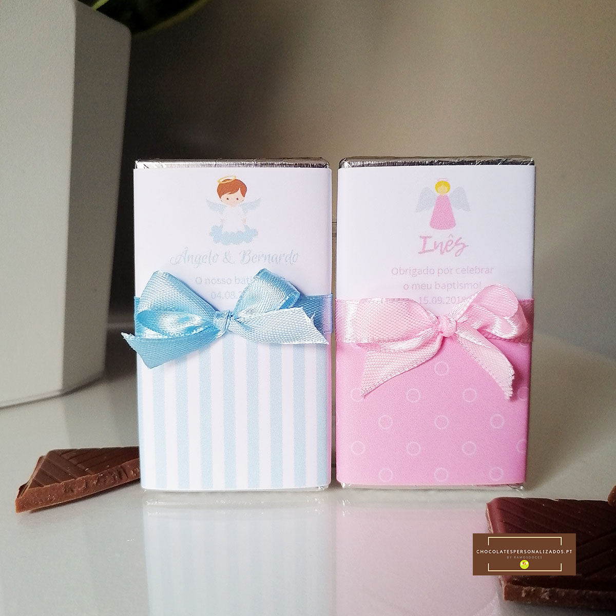Dois tabletes de chocolate com embalagem azul e rosa decoradas com laços e anjos