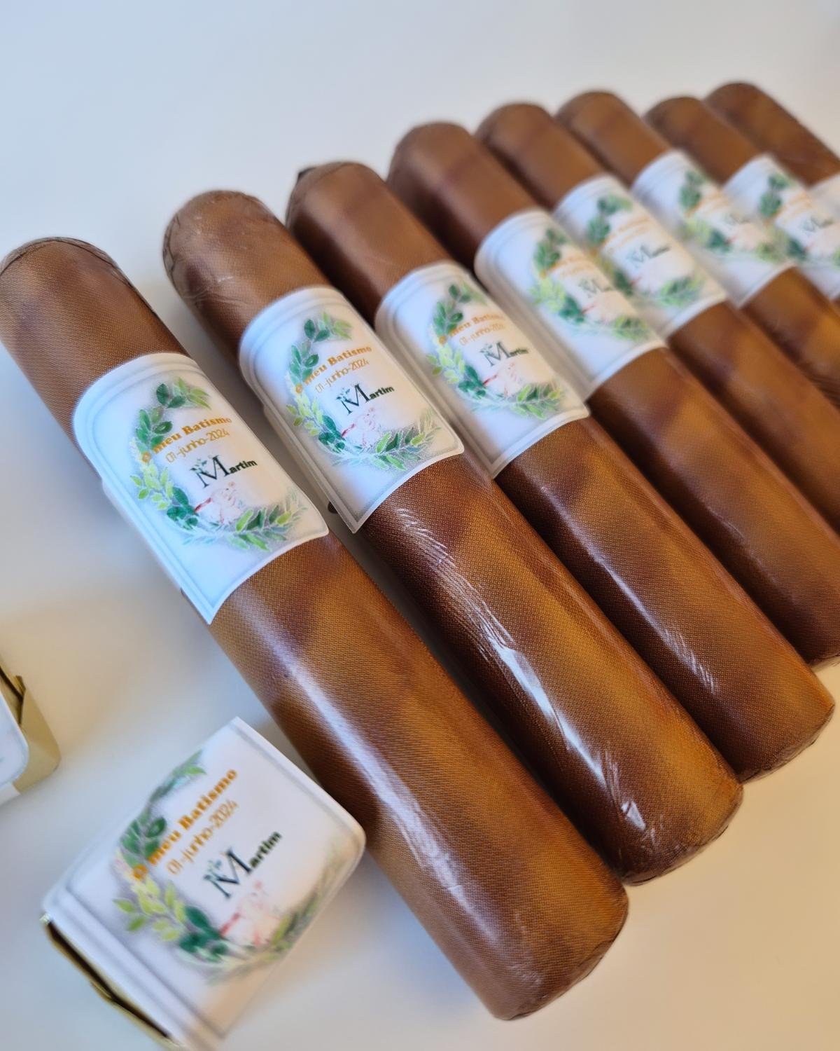 Tubos de couro castanho com etiquetas brancas e texto em português sobre superfície clara