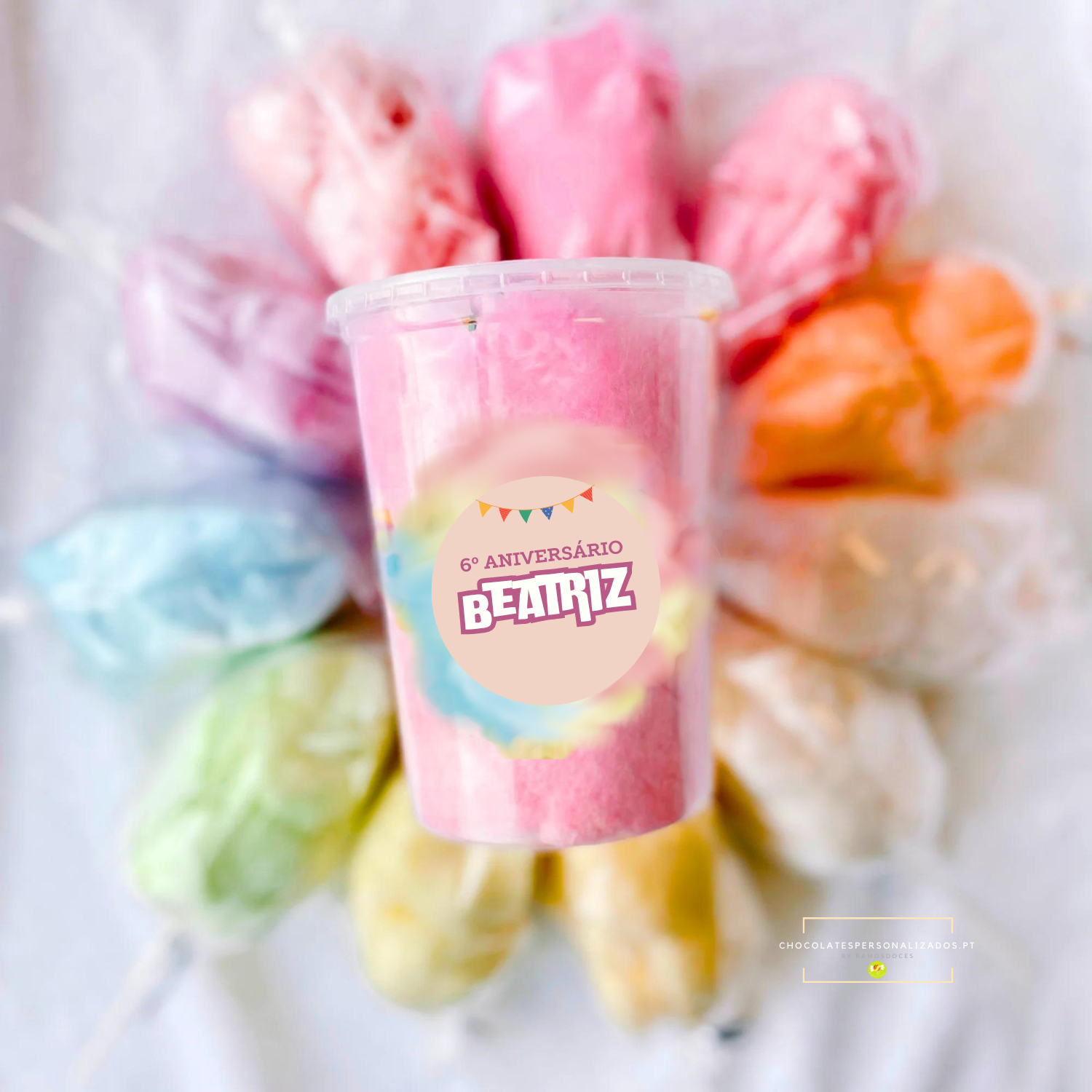 Embalagem de algodão doce rosa com etiqueta de aniversário rodeada por sacos de algodão doce colorido.