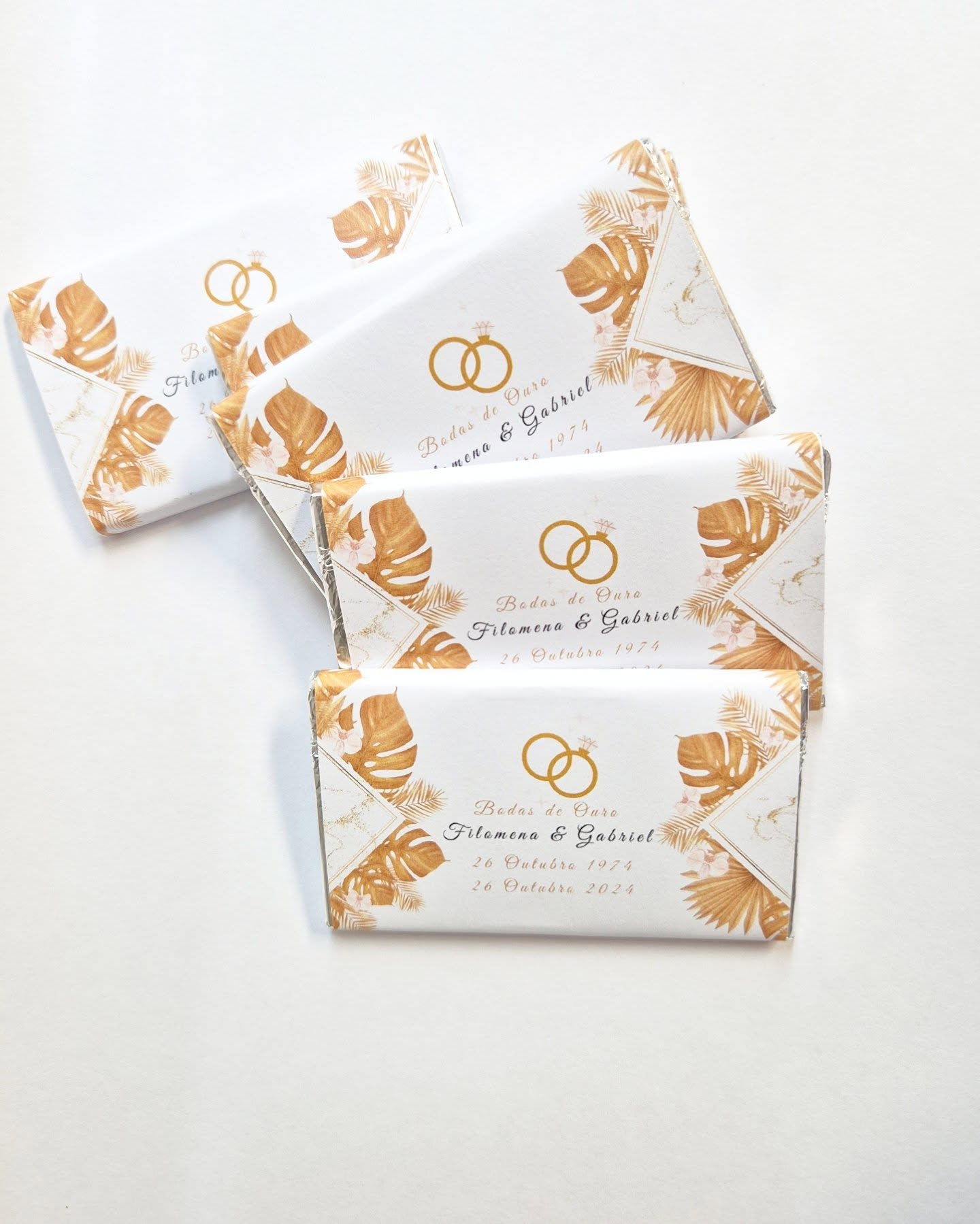 Barras de chocolate com embalagem branca decorada com folhas douradas e nomes de casamento