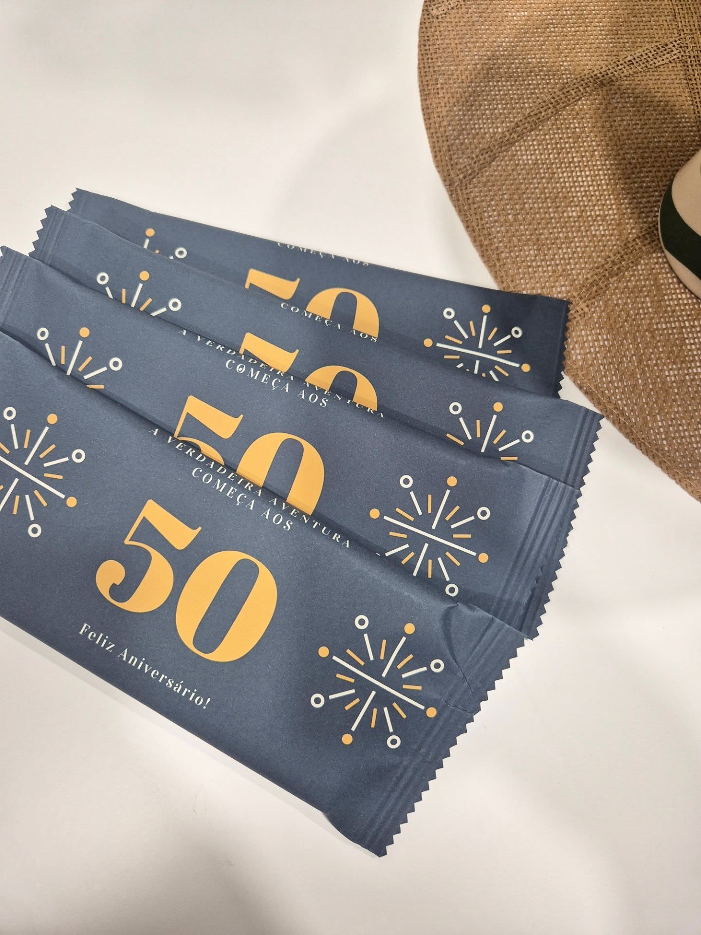 Embalagens azuis com 50 amarelo e texto Feliz Aniversário ao lado de chapéu de palha
