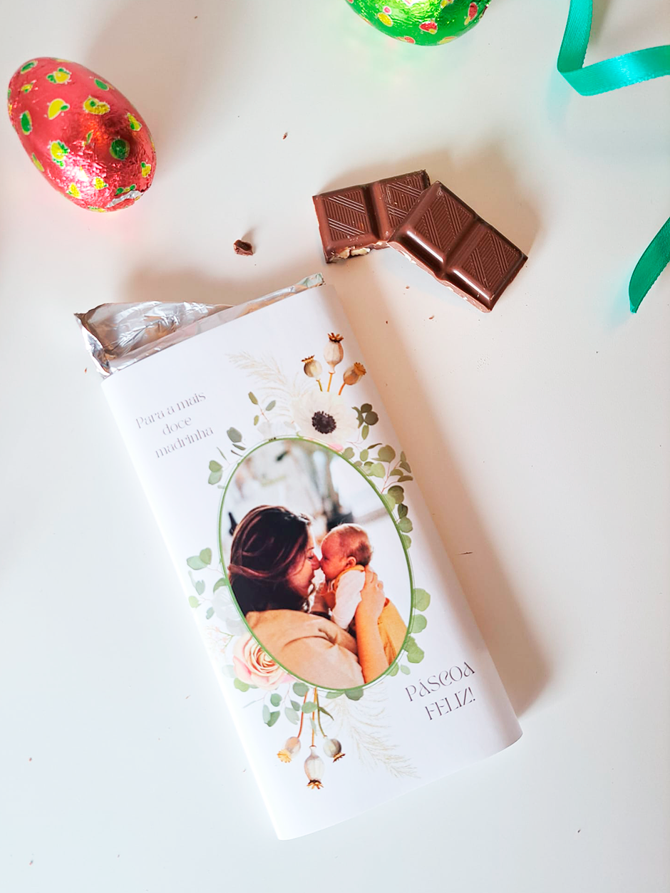 Barra de chocolate com embalagem decorada com foto de mãe e criança e texto de Páscoa, ovos de chocolate coloridos e fita verde.
