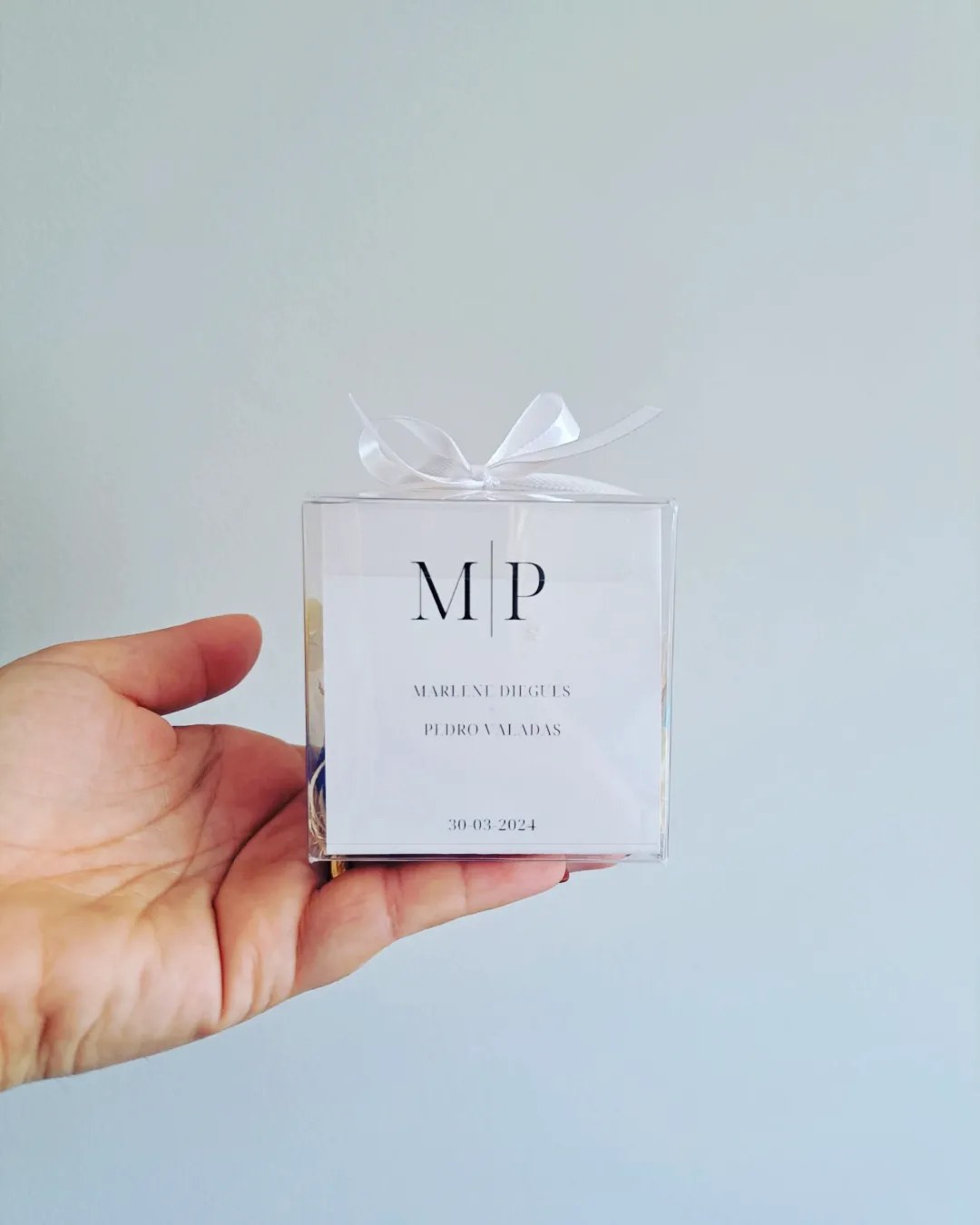 Caixa transparente com etiqueta branca e laço branco nas mãos