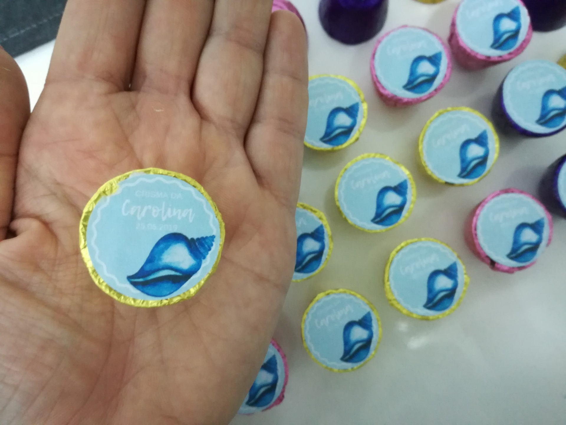 Pirulitos redondos com embalagem azul claro e concha azul, segurado na mão