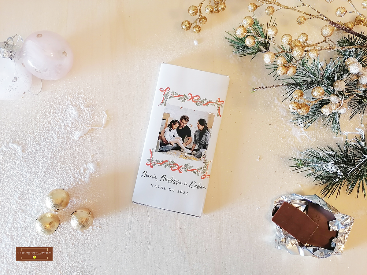 Embalagem de chocolate branca com foto e texto natalício, decorada com elementos dourados e pinheiro.