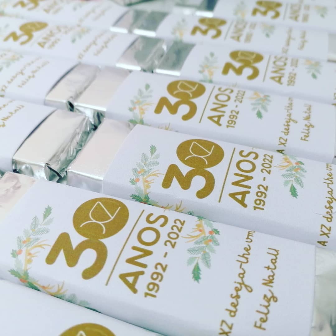 Barras de chocolate embrulhadas com design comemorativo de 30 anos em branco, dourado e verdes.