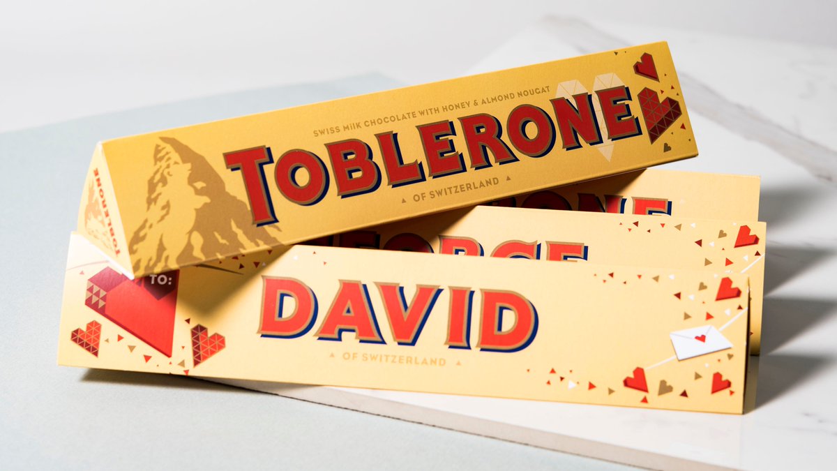 Caixas de Toblerone amarelas com personalização 'DAVID' e detalhes de corações e cartas.