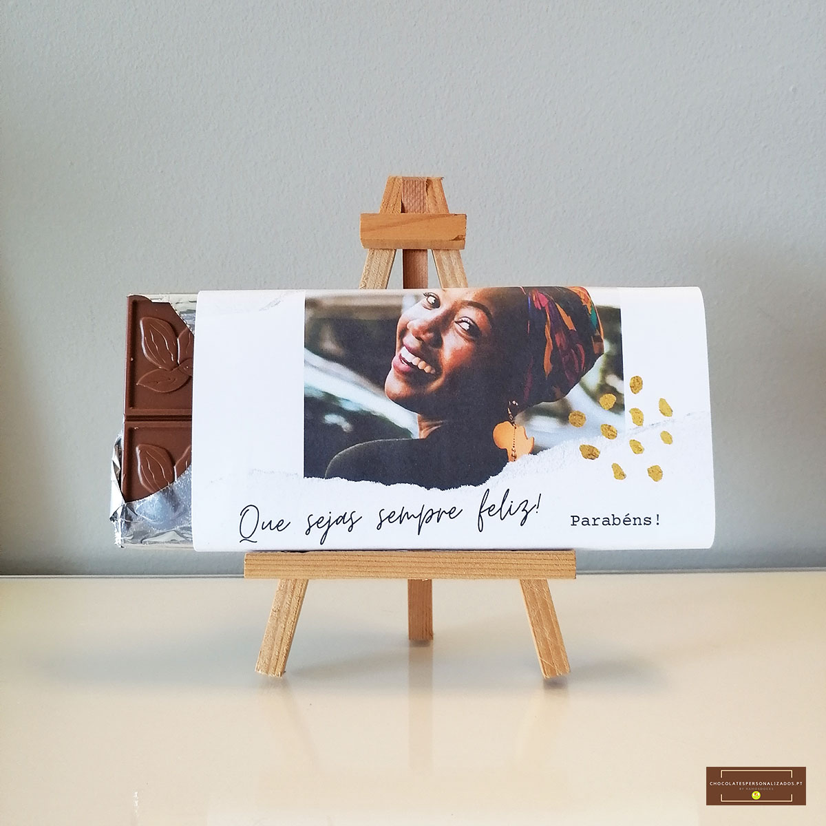 Tablete de chocolate com embalagem branca e fotografia de mulher sorridente em mini cavalete