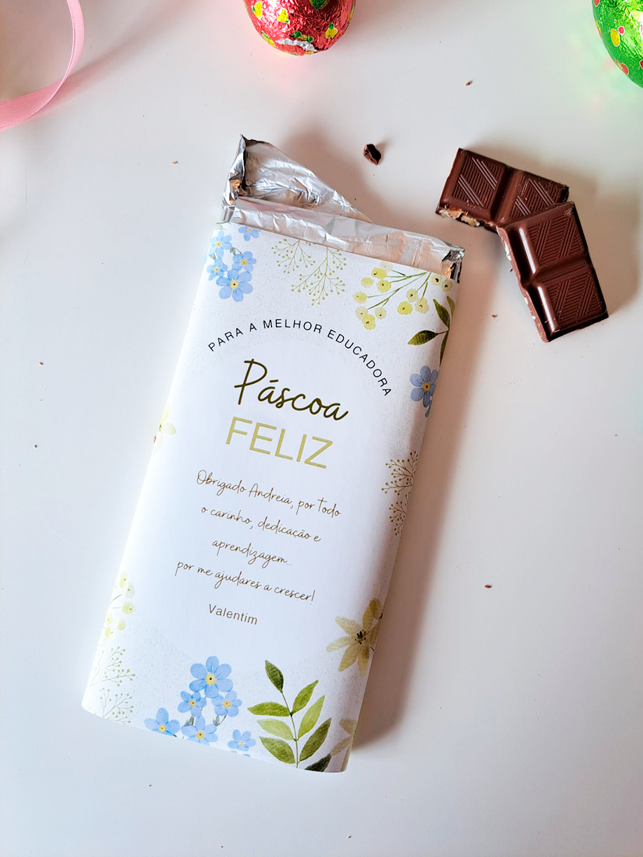 Barra de chocolate com embalagem floral e texto em português, com pedaços de chocolate ao lado.