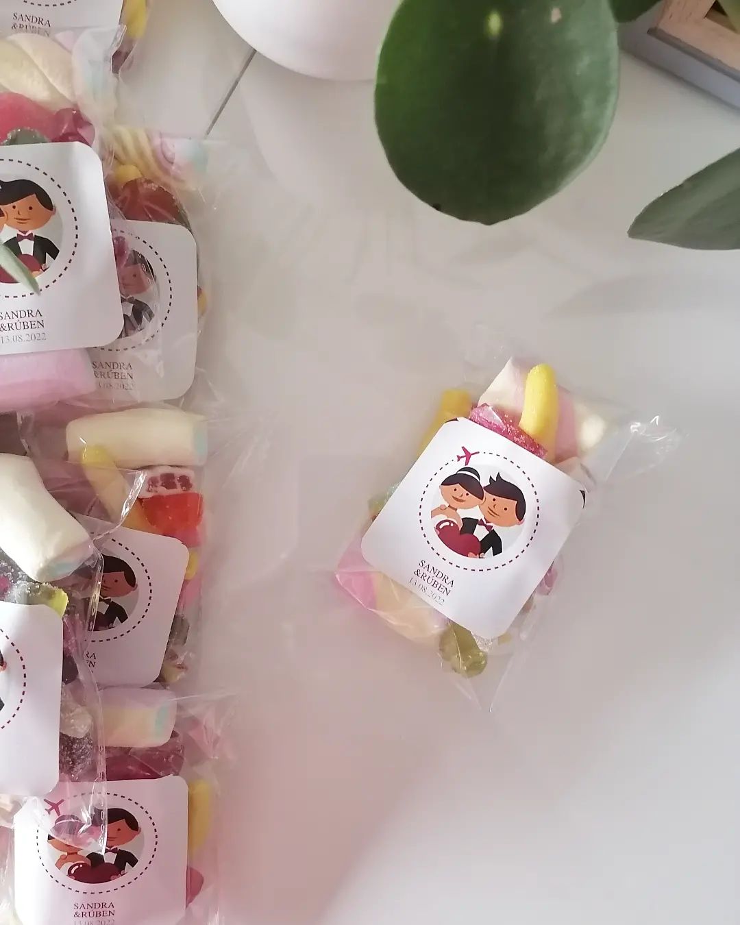 Pacotes pequenos de doces em saquinhos transparentes com etiquetas brancas ilustradas sobre mesa branca