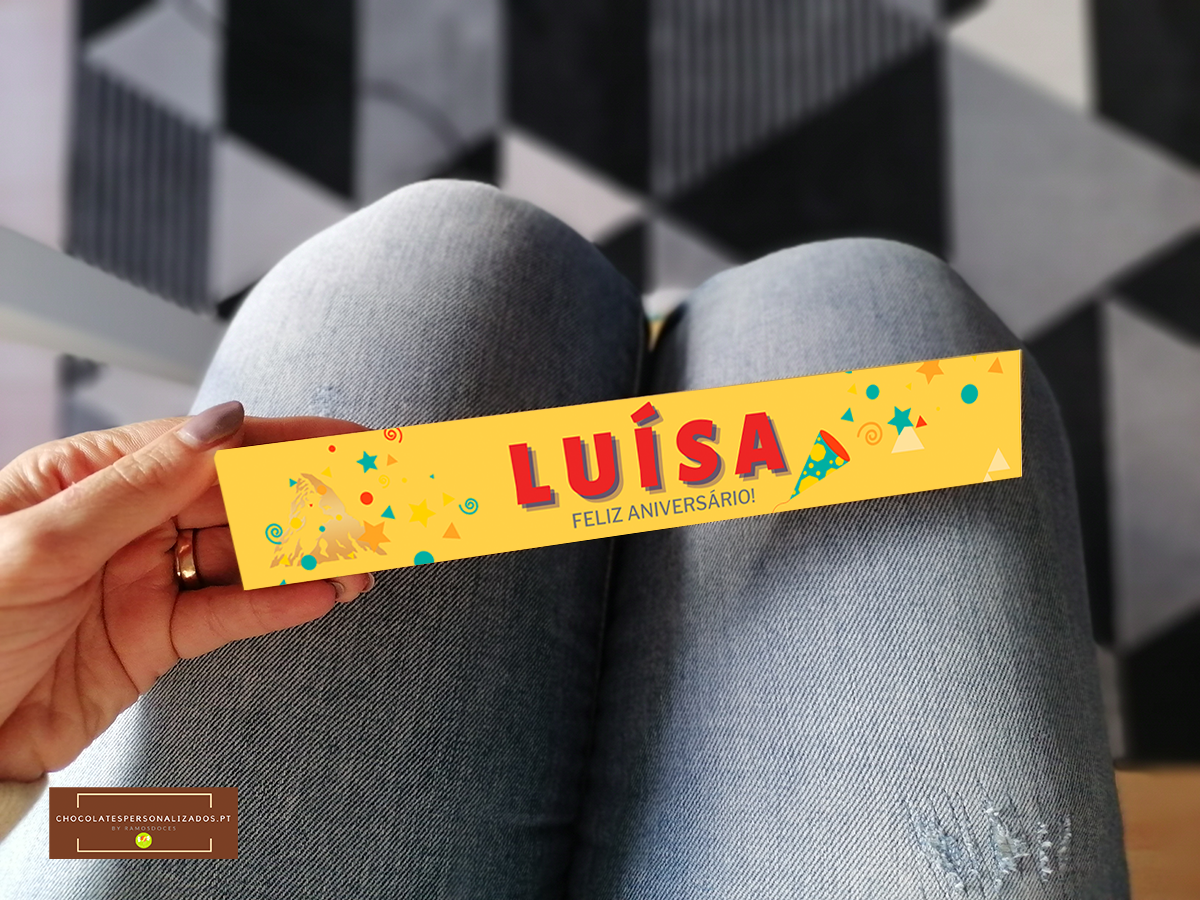Pulseira amarela de festa com texto LUÍSA FELIZ ANIVERSÁRIO sobre jeans azul claro