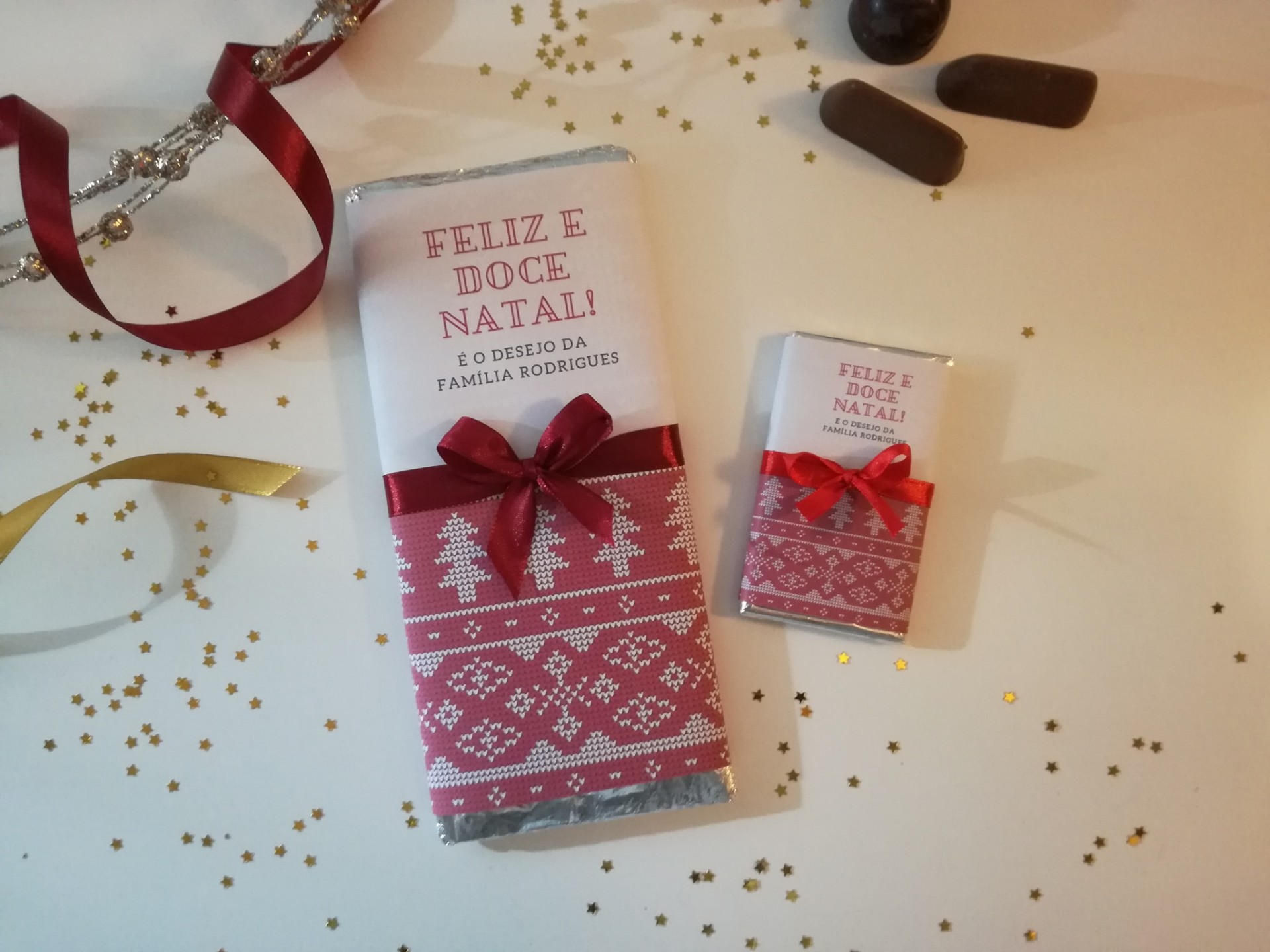 Dois chocolates embrulhados para Natal com mensagem e laços vermelhos sobre fundo branco decorado