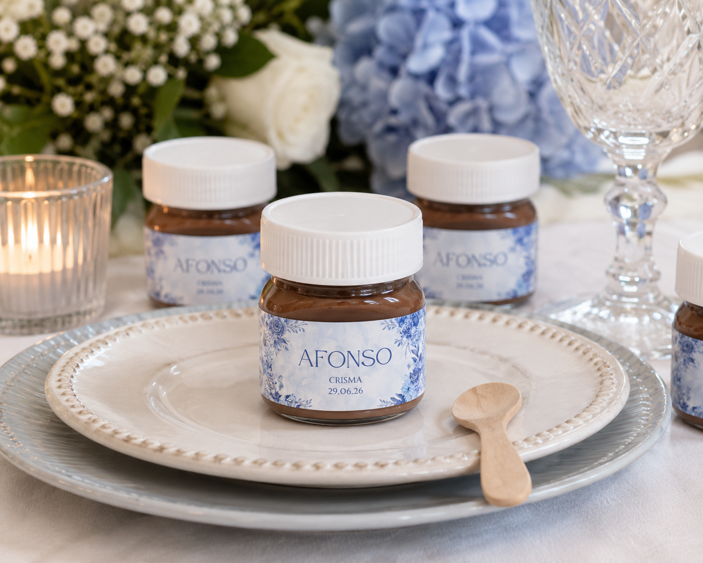 Frascos pequenos com creme castanho, etiqueta branca e azul com texto Afonso Crisma 29.06.26 em pratos com colher de madeira e decoração floral