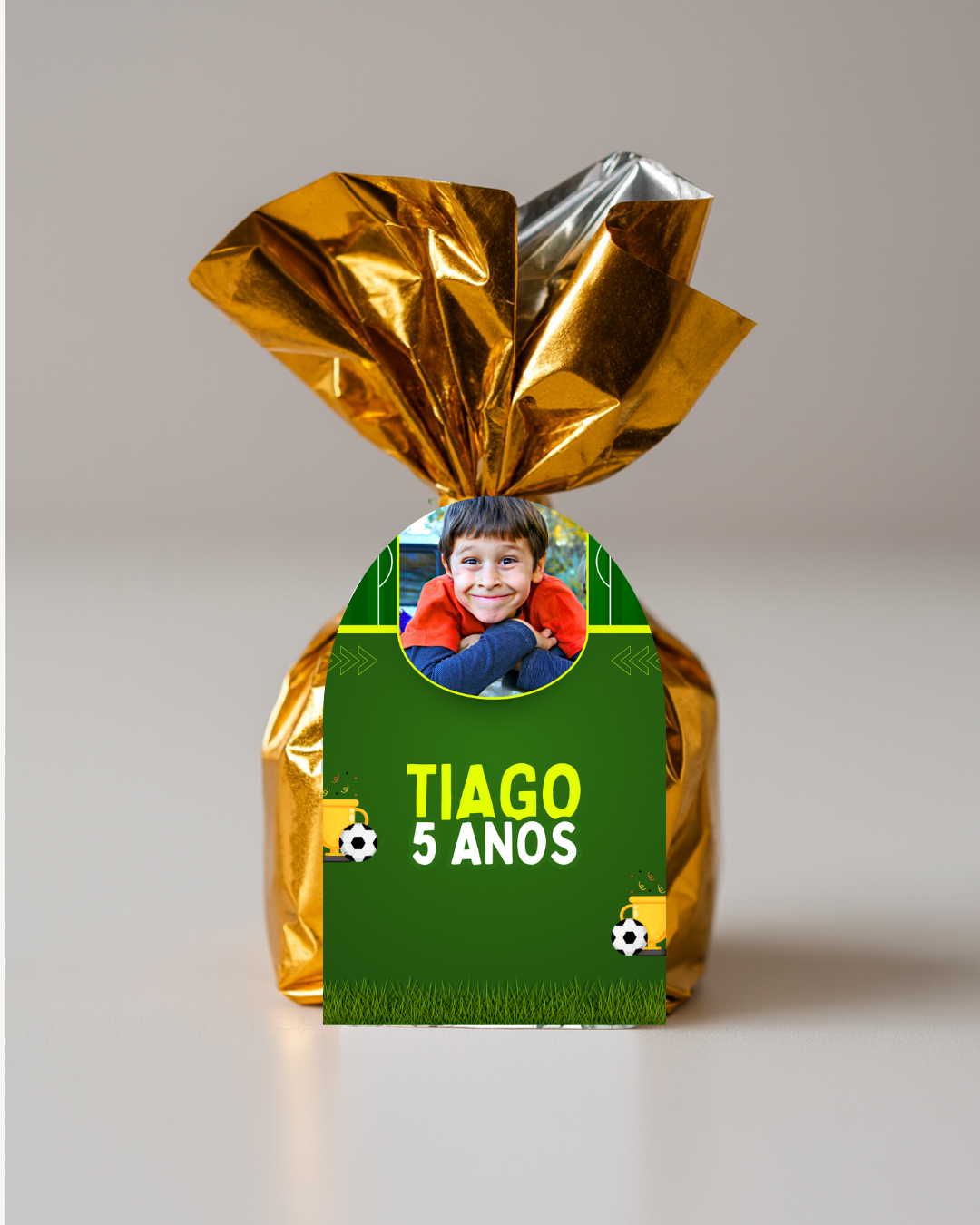Embalagem dourada com etiqueta verde e foto de criança com texto 'TIAGO 5 ANOS'