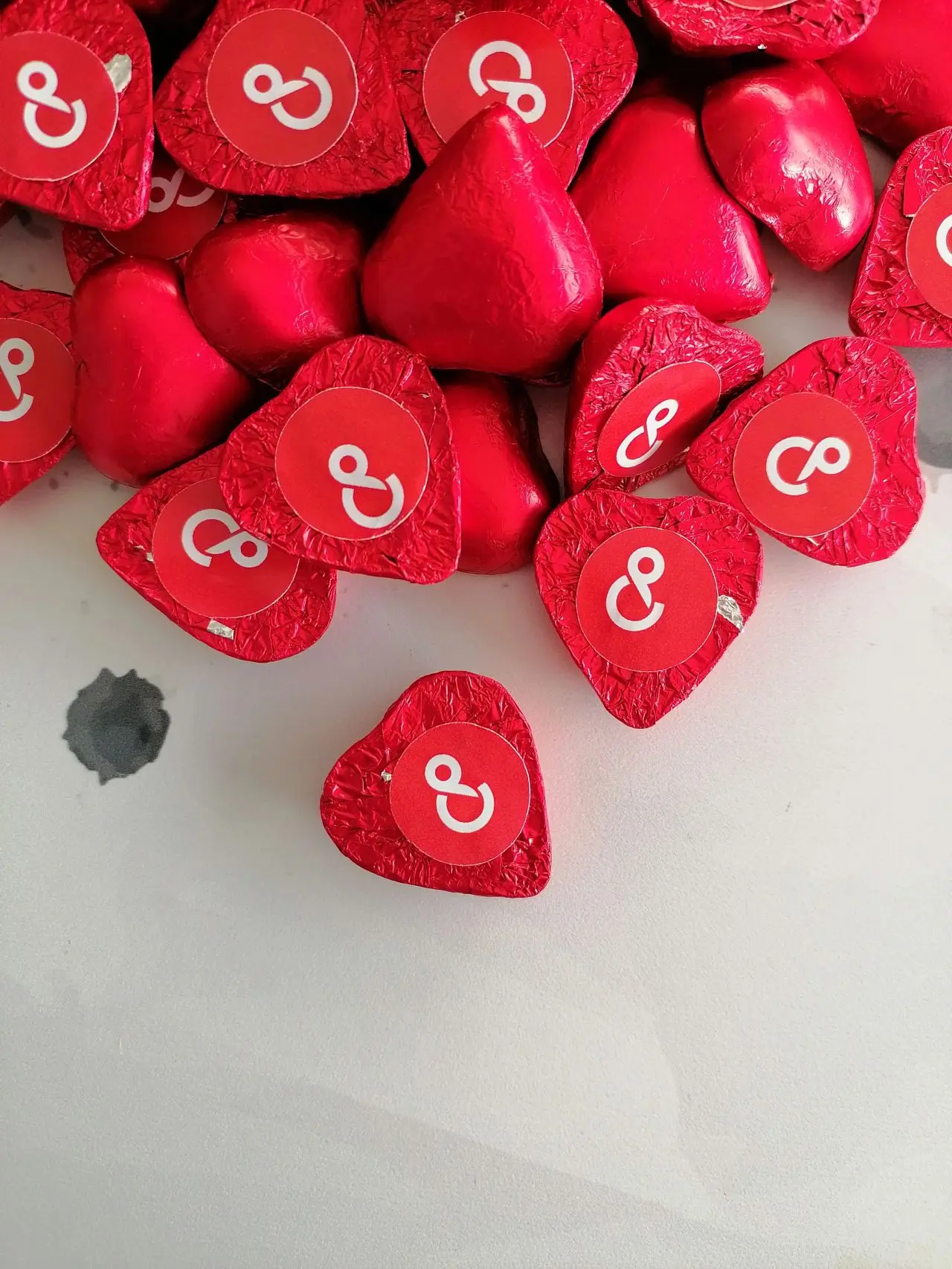 Chocolates em forma de coração embalados em papel vermelho com símbolos brancos sobre fundo branco