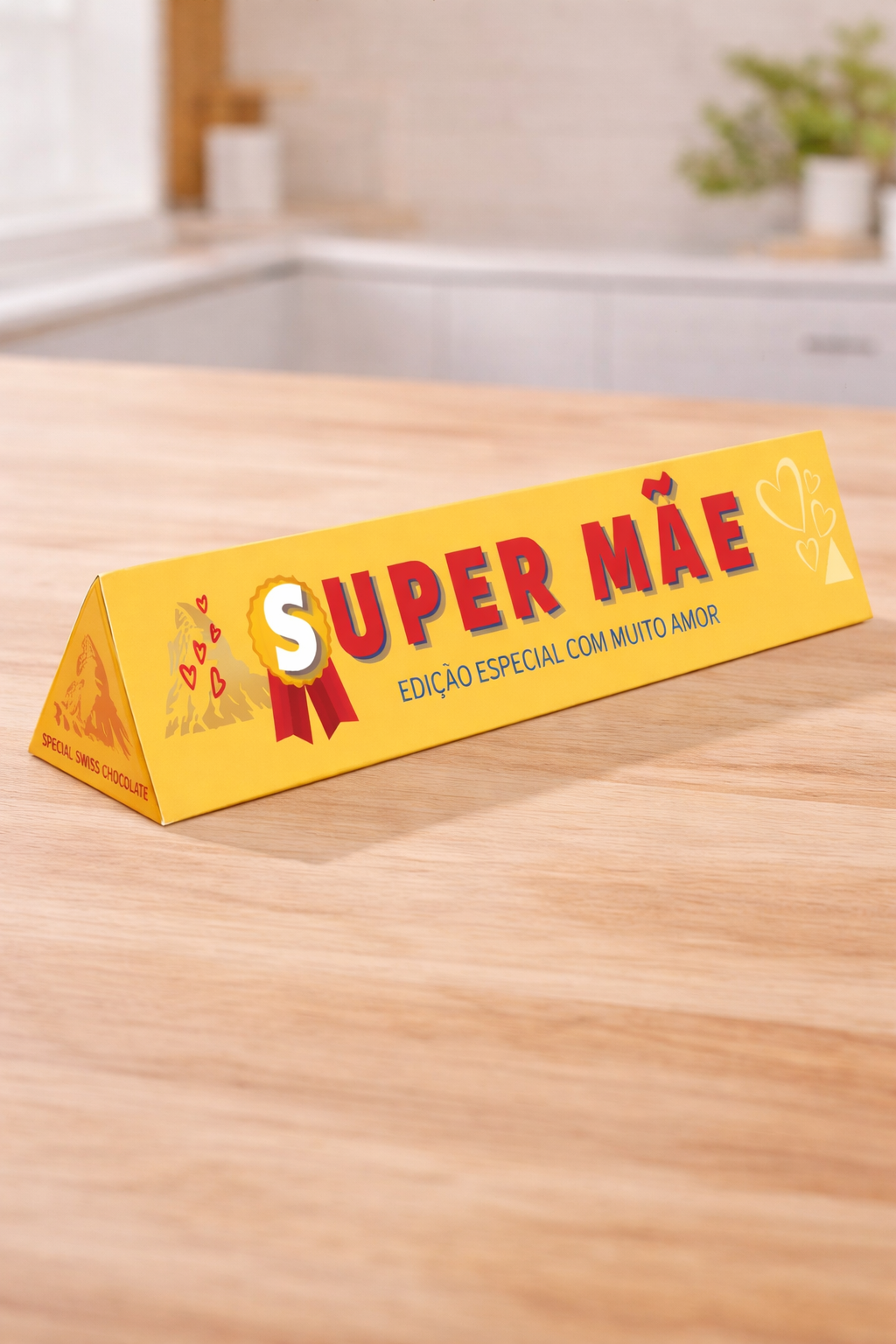 Embalagem amarela triangular de chocolate com texto SUPER MÃE sobre superfície de madeira