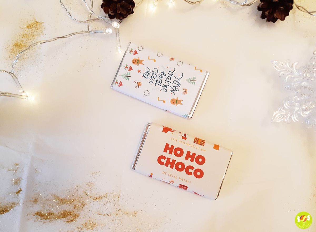 Duas caixas de chocolate natalícias com decorações coloridas sobre superfície branca com luzes e pinhas