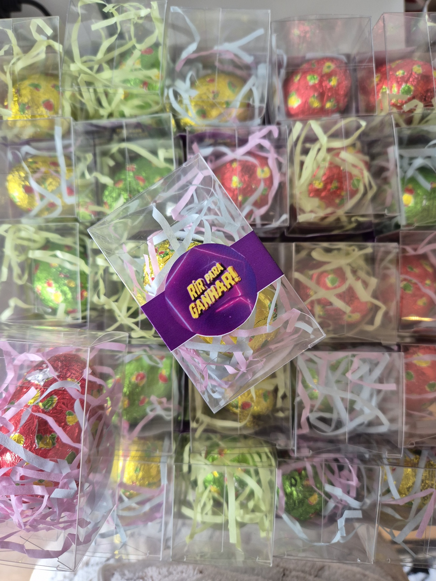 Caixas transparentes com ovos decorativos coloridos e etiqueta roxa com texto em português