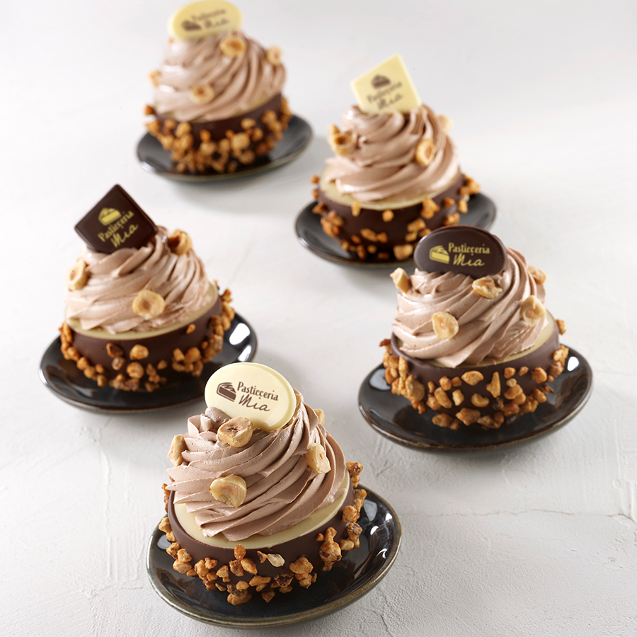Cinco cupcakes decorados com chocolate, creme castanho e avelãs em pratos pretos