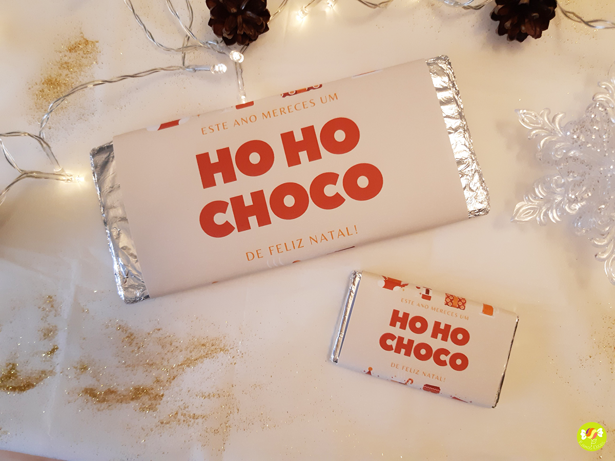 Duas barras de chocolate com texto HO HO CHOCO em embalagens brancas e vermelhas sobre superfície decorada