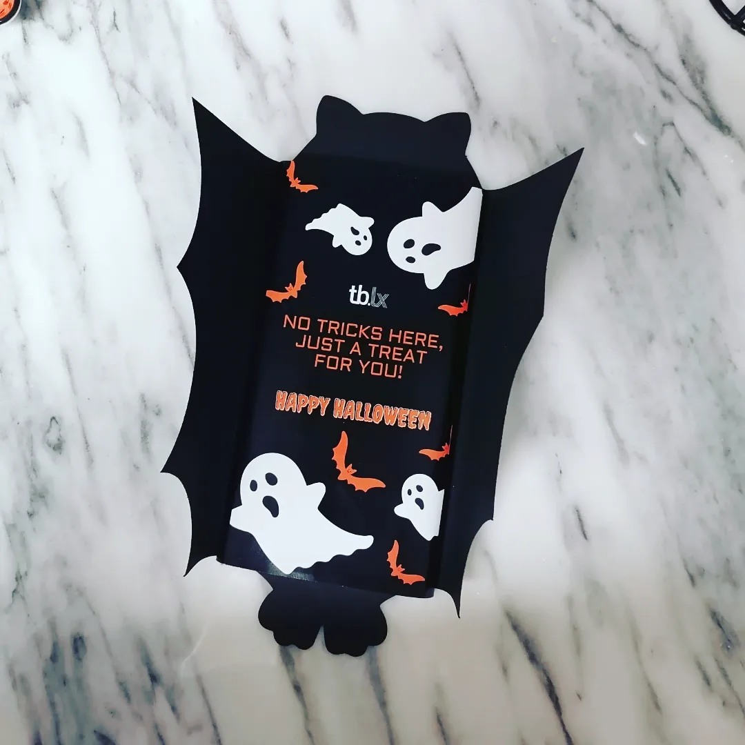 Embalagem preta de Halloween com fantasmas brancos, morcegos laranja e texto em laranja e branco