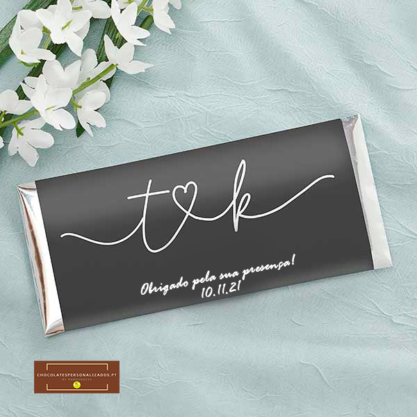 Barra de chocolate com embalagem preta e texto branco num tecido azul claro com flores brancas