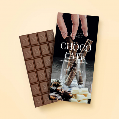 Barra de chocolate com embalagem preta mostrando texto e imagem de mãos segurando barras de chocolate enroladas em copo