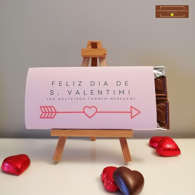 Barra de chocolate com embalagem rosa e texto de Feliz Dia de S. Valentim em cavalete de madeira com chocolates em forma de coração