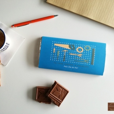 Barra de chocolate azul, pedaços de chocolate, caneca de café, caneta e caderno sobre superfície branca