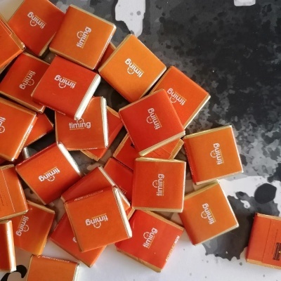 Pequenos chocolates quadrados com embalagem laranja 'timing' sobre superfície preta e branca
