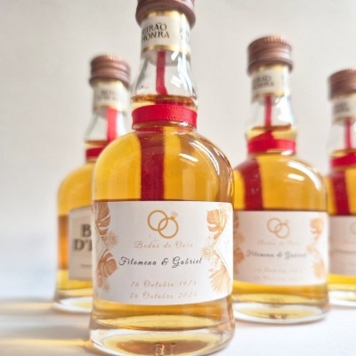 Garrafas pequenas de vidro com líquido amarelo e etiquetas de Bodas de Ouro