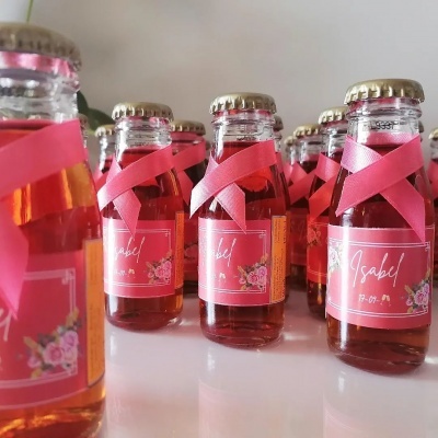 Garrafas pequenas de vidro com fita rosa e etiquetas com nome Isabel
