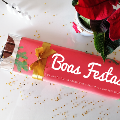 Barra de chocolate embalada com papel vermelho com texto 'Boas Festas' e decoração natalícia