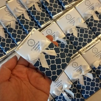 Caixas pequenas azuis com padrão branco, laço branco e cartão com texto são mostradas em fileiras.