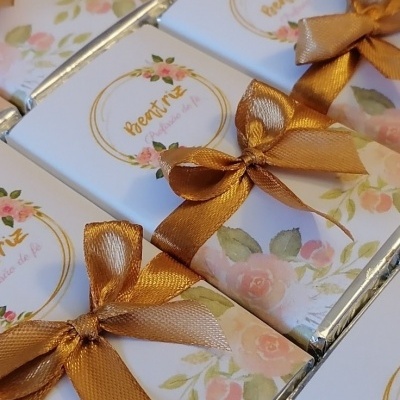 Chocolates embrulhados com papel branco floral e laços dourados