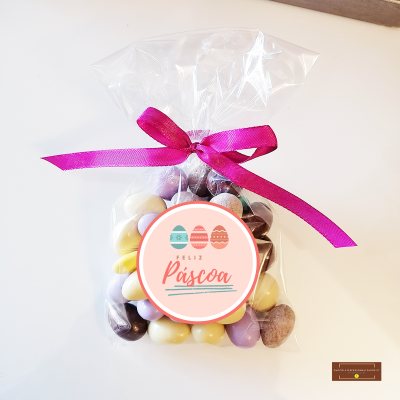 Saco transparente com amêndoas coloridas e laço rosa com etiqueta FELIZ Páscoa