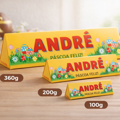 Três caixas triangulares amarelas com design de Páscoa e texto André Páscoa Feliz em diferentes tamanhos e pesos sobre mesa de madeira.