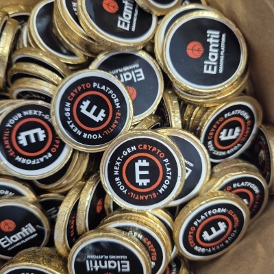 Moedas metálicas douradas com emblemas pretos contendo texto sobre plataforma de criptomoedas dentro de recipiente de papel castanho