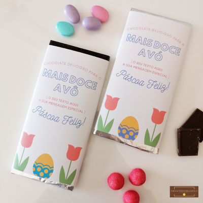 Duas barras de chocolate com embalagens brancas decoradas com texto em português e desenhos de Páscoa, junto a pequenos ovos de chocolate coloridos.