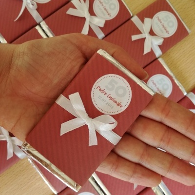 Barras de chocolate personalizadas com laço branco e etiqueta, em fundo de mesa de madeira.