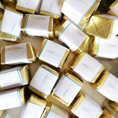 Pequenas embalagens de chocolates quadrados em papel dourado com rótulos brancos com texto 'sonthemeu'
