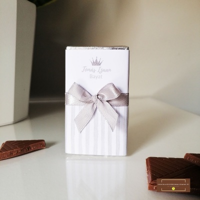 Embalagem branca com laço prateado e pedaços de chocolate ao leite.