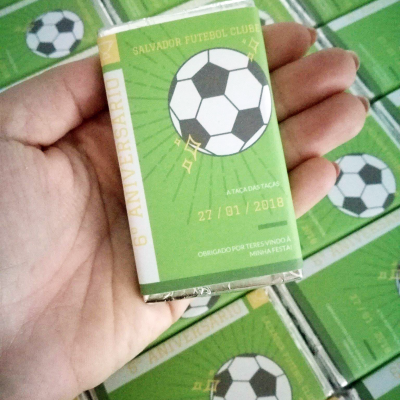 Caixa pequena verde com bola de futebol e texto em português, em mão sobre várias caixas iguais