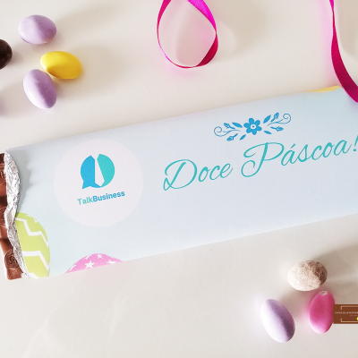 Barra de chocolate com embalagem azul claro e texto 'Doce Páscoa!', amêndoas de chocolate coloridas e fita rosa