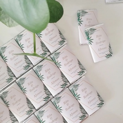 Lembranças de um Casamento Batizado inspirado na Natureza Pequenas embalagens brancas com texto 'Rita & Rodrigo e Afonso' e folhas verdes