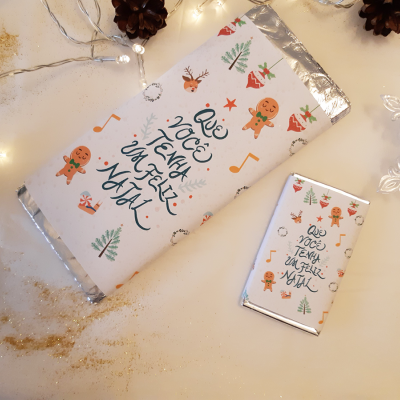 duas barras de chocolate festivas com decoração natalícia e texto inspirador numa superfície clara com luzes de natal