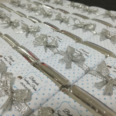 Barras de chocolate embrulhadas com papel branco e bolinhas azuis, laços prateados e etiquetas para batismo
