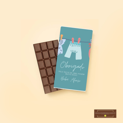 Barra de chocolate com embalagem azul com ilustrações de roupa de bebé e texto de agradecimento em português.