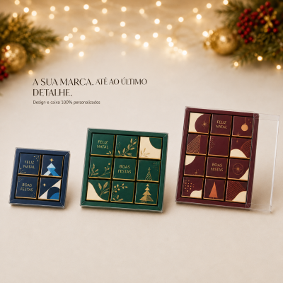 Caixas transparentes com chocolates decorados em papel azul, verde e vermelho com mensagens natalinas e decoração festiva ao fundo